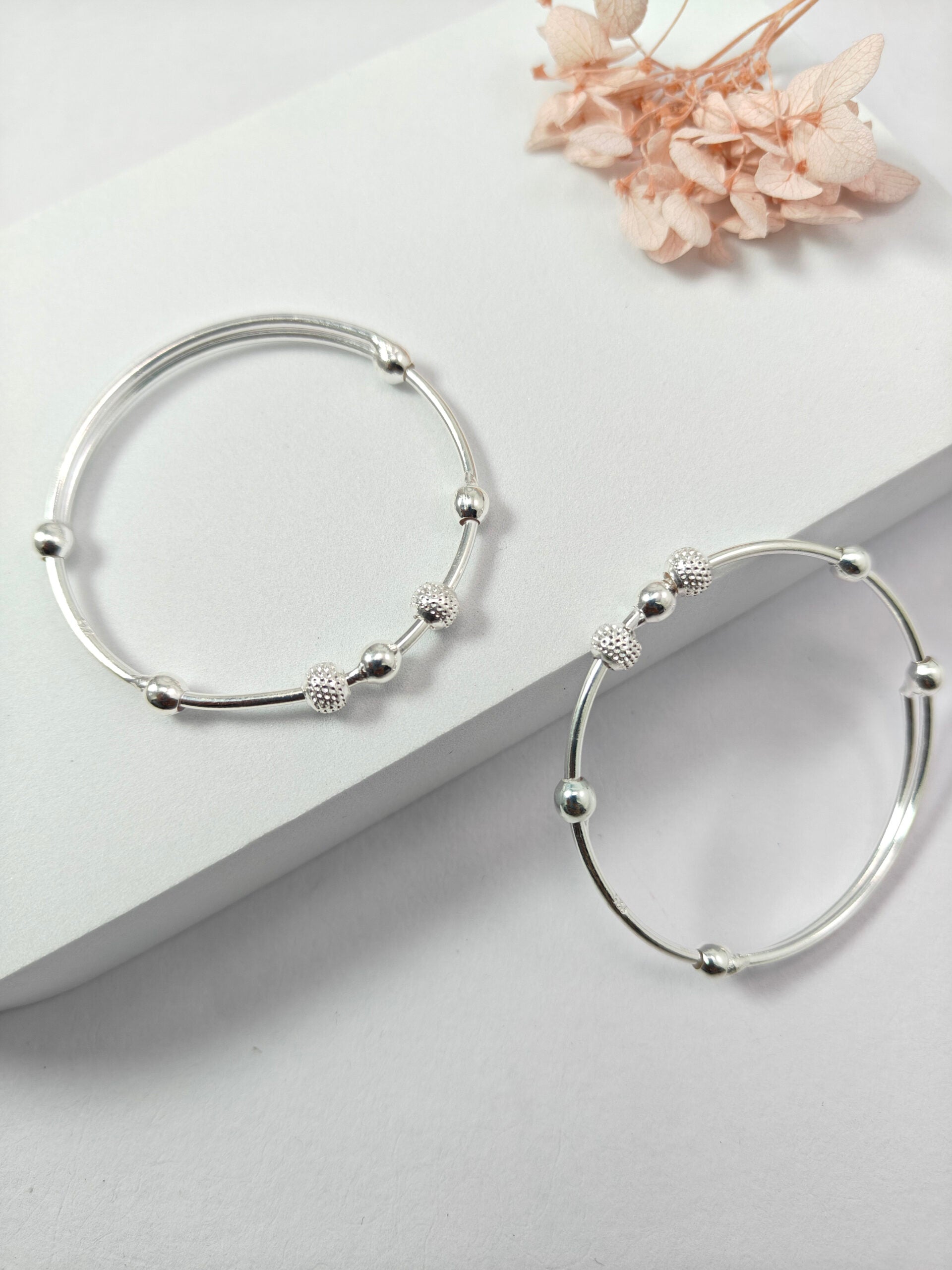 Silver hoop earrings with bead detailing on a light gray surface with dried flowers.